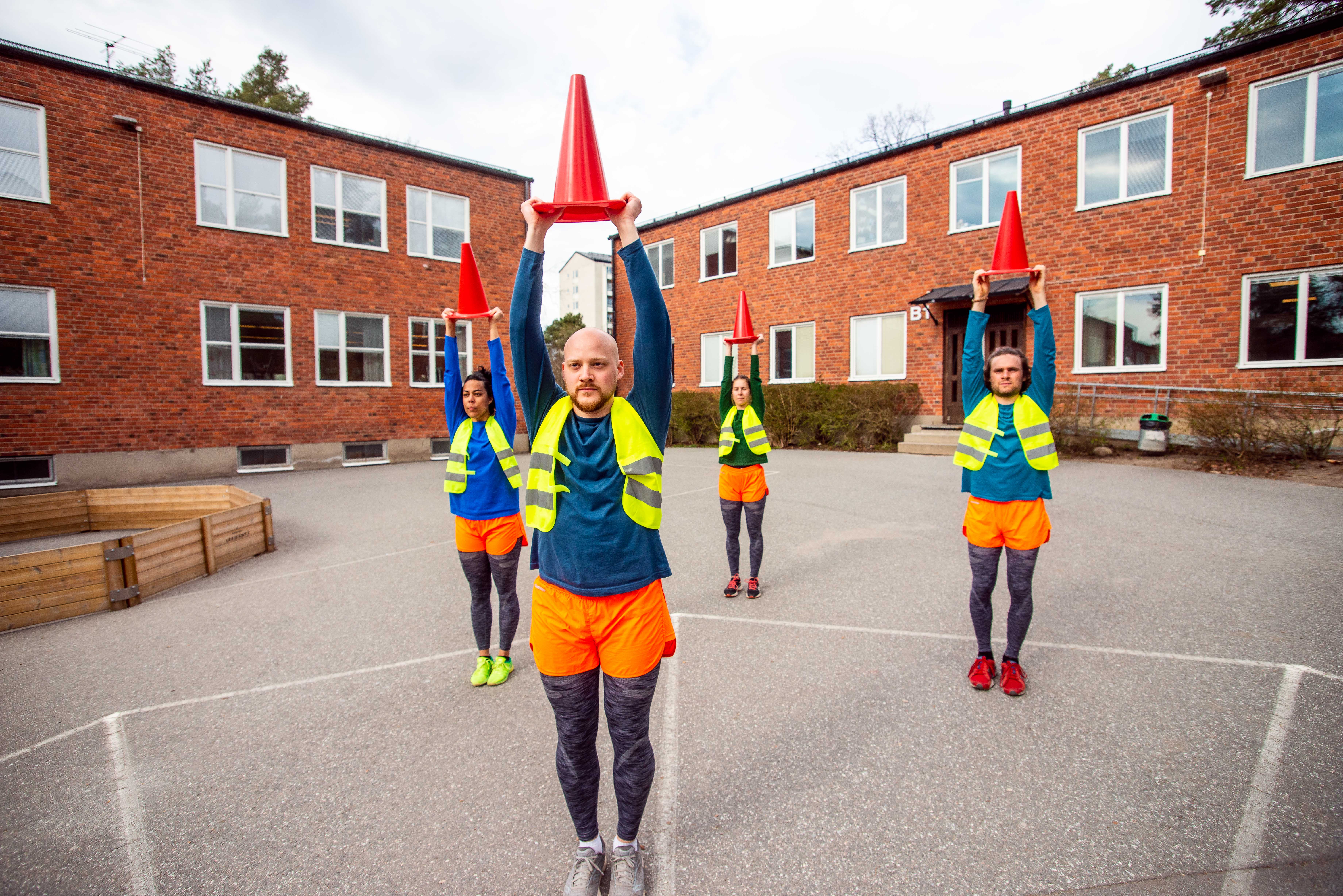 Fyra personer med reflexvästar och färgglada kläder håller i trafikkoner.