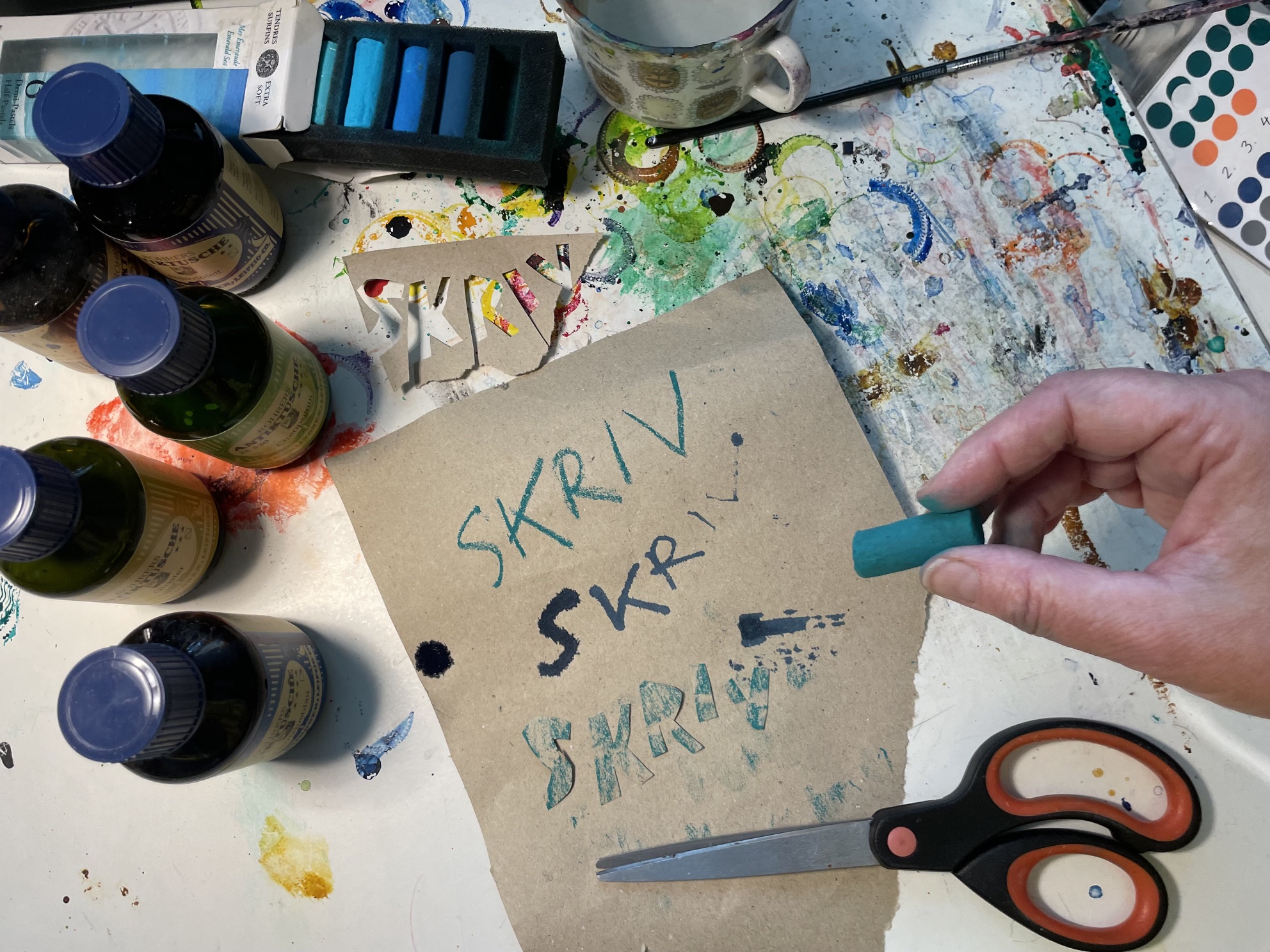 Ett rörigt skrivbord där texten "skriv" är skriven på olika sätt, med bläck, med krita och med pappersbitar. 
