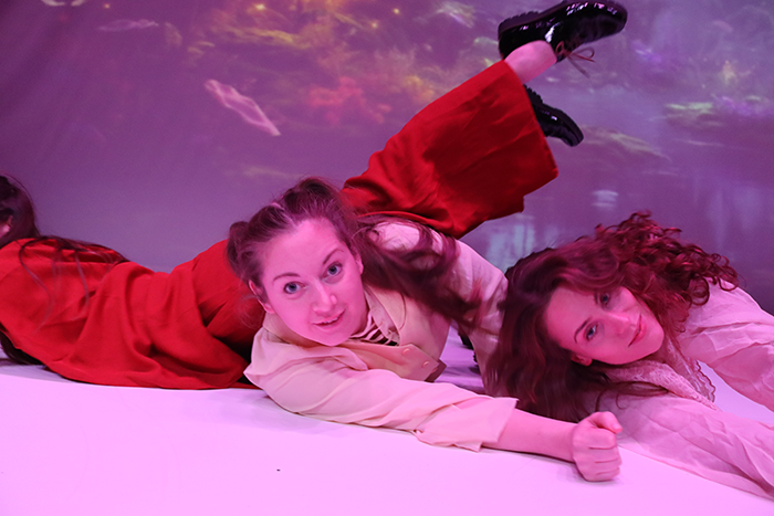 En rosa bakgrund och tre personer ligger på golvet och kollar in i kameran. 