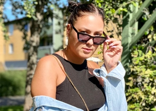 En person kollar in i kameran. Hon har solglasögon på sig. 